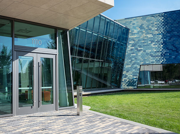 Modern building entrance with glass doors, angled glass facade, and blue tiled exterior wall